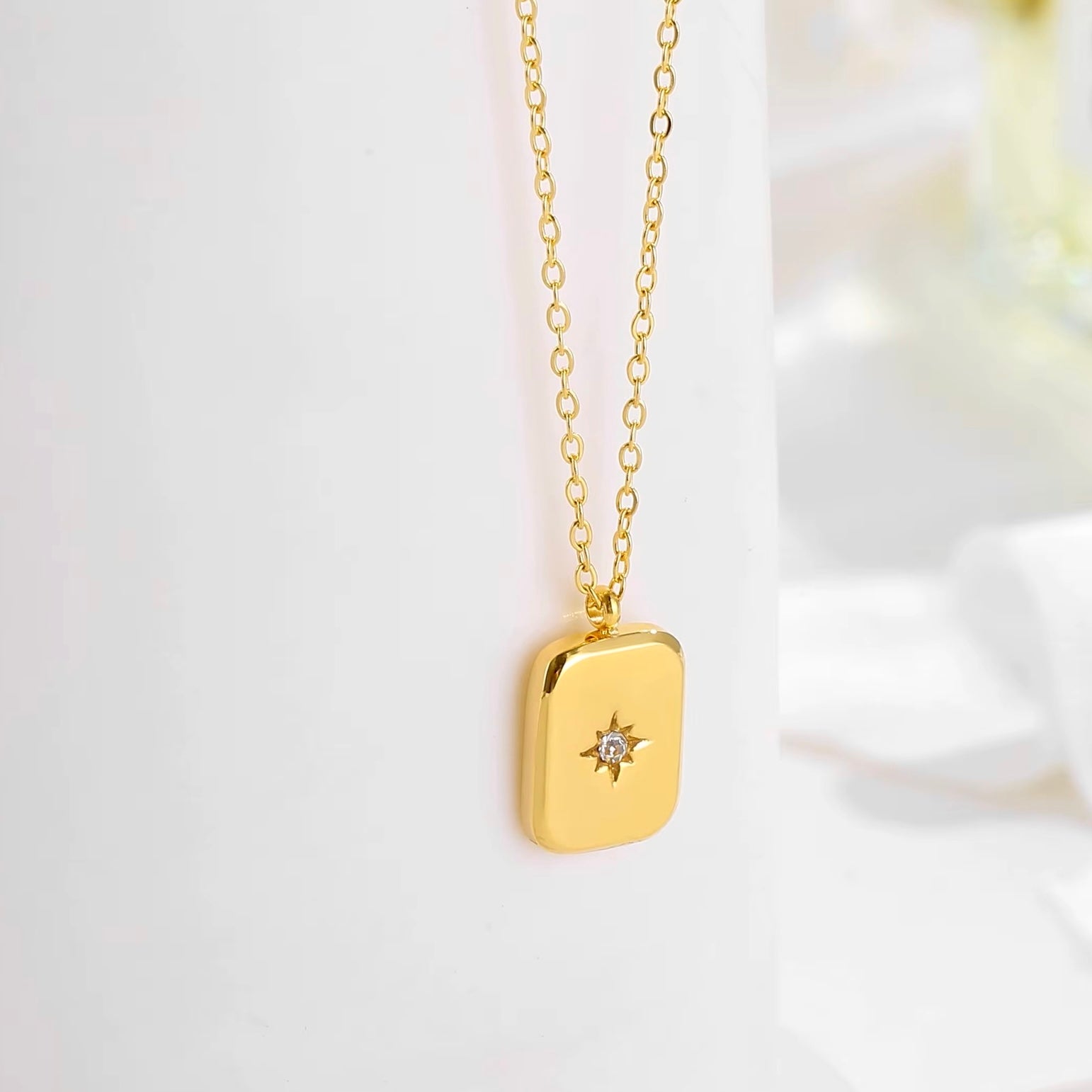 Minimalist gold pendant necklace featuring a rectangular design with a central cubic zirconia stone, inspired by the North Star