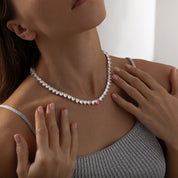 A sparkling silver-plated tennis-style necklace elegantly displayed on a soft, light background. It features a continuous row of heart-shaped cubic zirconia stones, each approximately 7 mm wide, set in rhodium-plated brass. The centerpiece is a single blush-pink heart stone (about 8 mm) that adds a pop of colour. The hearts are closely linked, creating a seamless chain around the neckline, and the full length is approximately 44 cm (17.5”) with a short extender. The polished silver setting enhances the bril
