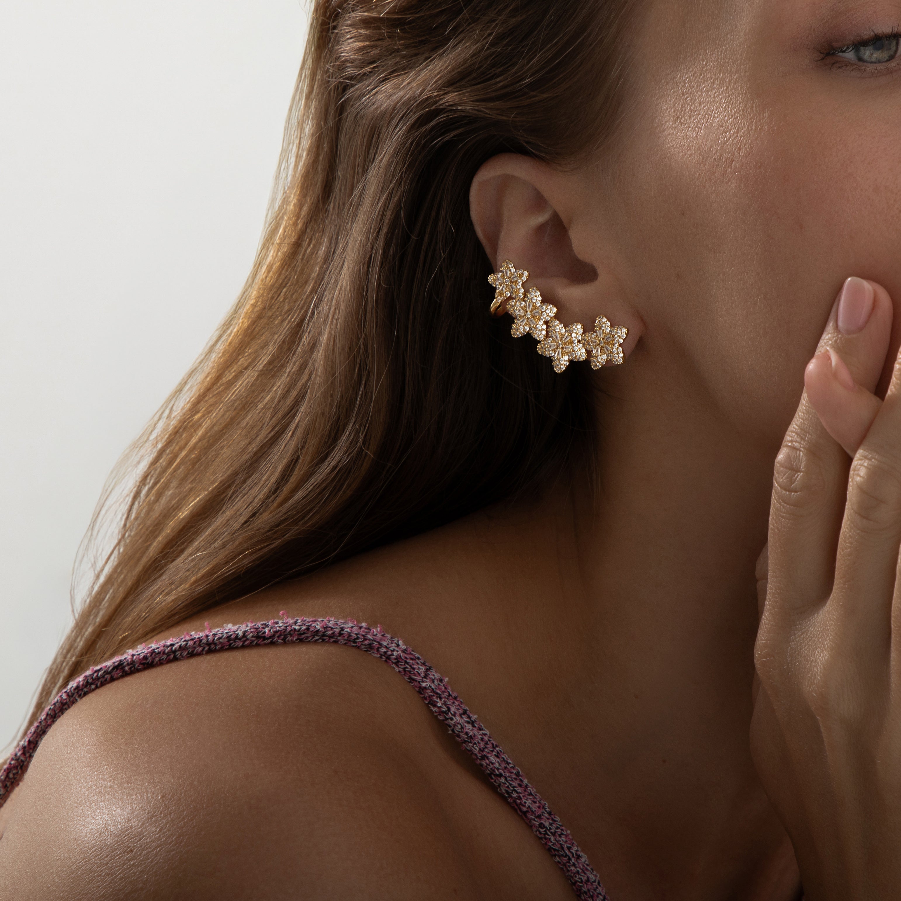 A pair of ear climbers designed to trace the curve of the earlobe, each featuring four small floral motifs graduating in size. Each flower is crafted in polished gold‑plated metal with delicate pavé-set round cubic zirconia centres and petals. The climbers measure approximately 4.1 cm in height and 2.3 cm in width, following the natural contour of the ear. They secure via a long, slightly curved post and a backing near the top flower to ensure a snug upward fit. The combination of warm gold and sparkling st