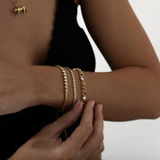 Close-up of a person's arm wearing gold bracelets with a neutral background
