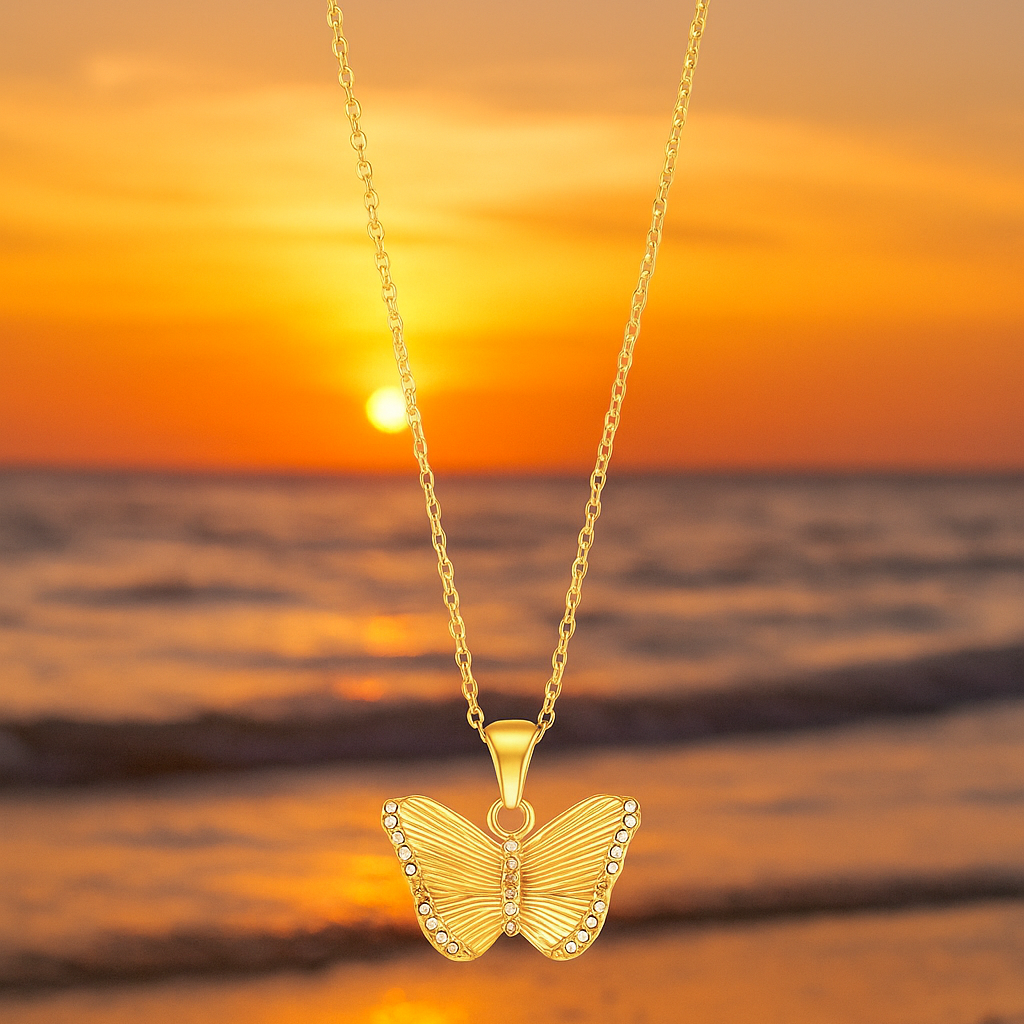 A delicate gold chain holds an ornate butterfly pendant approximately 2 cm wide. The butterfly features intricate filigree wings with openwork lattice and engraved detailing, accented by polished raised areas that catch the light. The body is subtly raised and smooth, with curled antennae. The pendant hangs from a small, plain bail. The chain is a fine, reflective cable‑style with tiny boxed links, fastened via a spring‑ring clasp. Overall, the piece exudes an elegant, vintage-inspired charm, blending airy