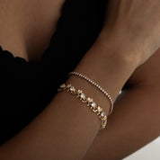 A delicate gold‑plated link bracelet featuring a whimsical parade of stylised elephant silhouettes, each linked trunk-to-tail. The small elephant charms are uniformly sized with softly rounded bodies and upturned trunks, creating a playful, continuous chain. The bracelet is secured with an integrated box‑style clasp and lays flat when worn, measuring around 18 cm in length. The polished gold finish gives a warm, refined sheen, enhancing its charming, artisan-crafted look.