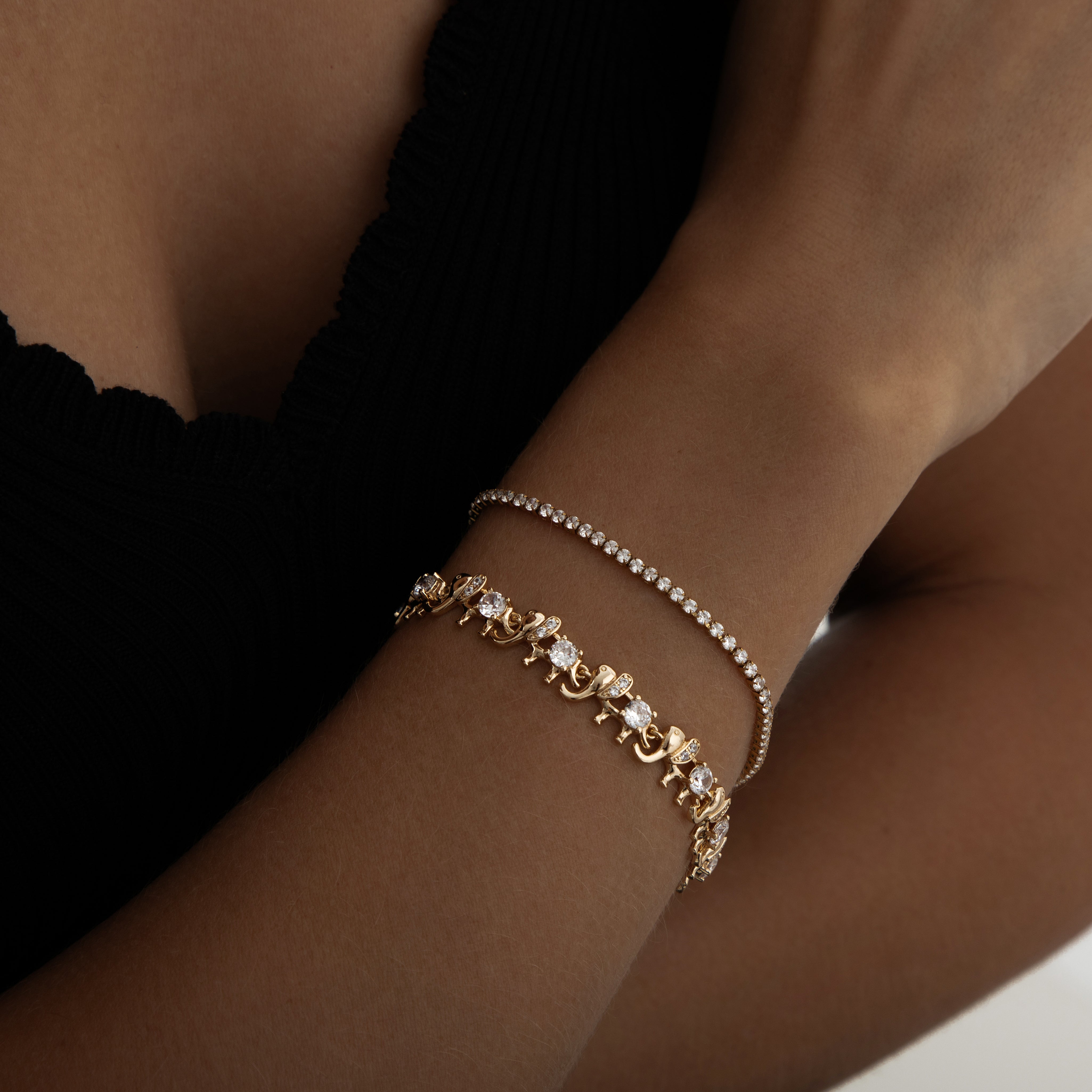 A delicate gold‑plated link bracelet featuring a whimsical parade of stylised elephant silhouettes, each linked trunk-to-tail. The small elephant charms are uniformly sized with softly rounded bodies and upturned trunks, creating a playful, continuous chain. The bracelet is secured with an integrated box‑style clasp and lays flat when worn, measuring around 18 cm in length. The polished gold finish gives a warm, refined sheen, enhancing its charming, artisan-crafted look.