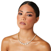 Model wearing a gold crystal tennis necklace featuring graduated cubic zirconia stones with pavé halos, styled with a minimalist outfit to highlight the necklace's elegant sparkle
