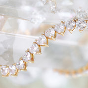 A deluxe tennis-style necklace composed of 7 mm heart-shaped clear cubic zirconia stones, each set in polished 18 ct gold plating. The hearts are aligned closely along a 16‑inch (40 cm) chain, creating a continuous sparkle around the neckline. The design features a secure, invisible clasp hidden behind one stone for a seamless look. The high-reflective gold finish and perfectly cut CZs give the piece a luxurious, radiant appeal—ideal for special occasions or elevating everyday style. It weighs approximately