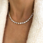 A deluxe tennis-style necklace composed of 7 mm heart-shaped clear cubic zirconia stones, each set in polished 18 ct gold plating. The hearts are aligned closely along a 16‑inch (40 cm) chain, creating a continuous sparkle around the neckline. The design features a secure, invisible clasp hidden behind one stone for a seamless look. The high-reflective gold finish and perfectly cut CZs give the piece a luxurious, radiant appeal—ideal for special occasions or elevating everyday style. It weighs approximately