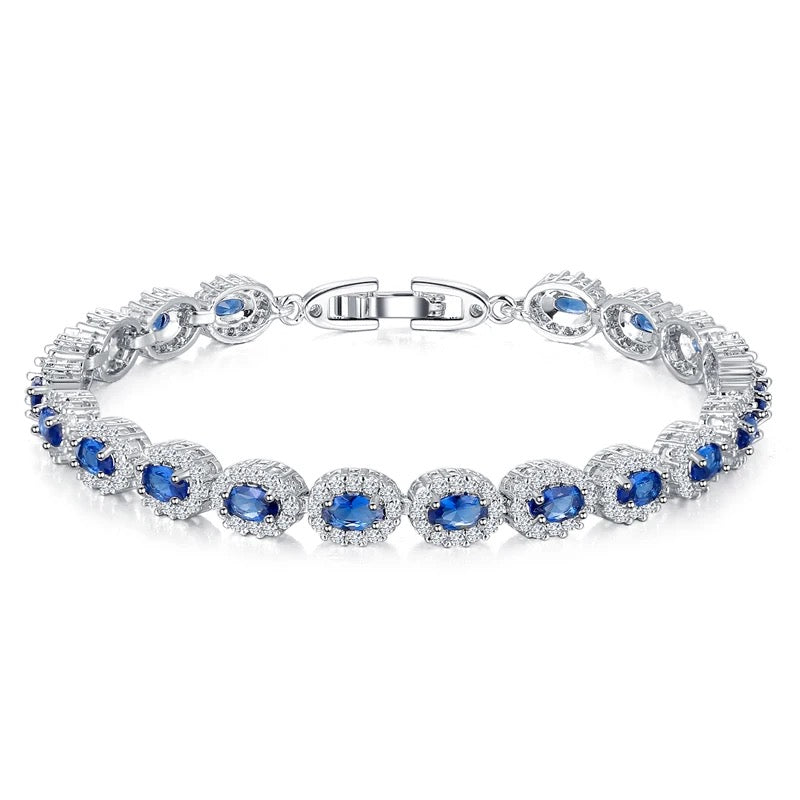 A silver tennis bracelet featuring oval cut blue crystals surrounded by white cubic zirconia.
