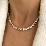 A deluxe tennis-style necklace composed of 7 mm heart-shaped clear cubic zirconia stones, each set in polished 18 ct gold plating. The hearts are aligned closely along a 16‑inch (40 cm) chain, creating a continuous sparkle around the neckline. The design features a secure, invisible clasp hidden behind one stone for a seamless look. The high-reflective gold finish and perfectly cut CZs give the piece a luxurious, radiant appeal—ideal for special occasions or elevating everyday style. It weighs approximately