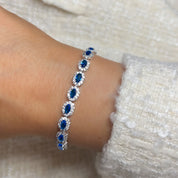 A silver tennis bracelet featuring oval cut blue crystals surrounded by white cubic zirconia.