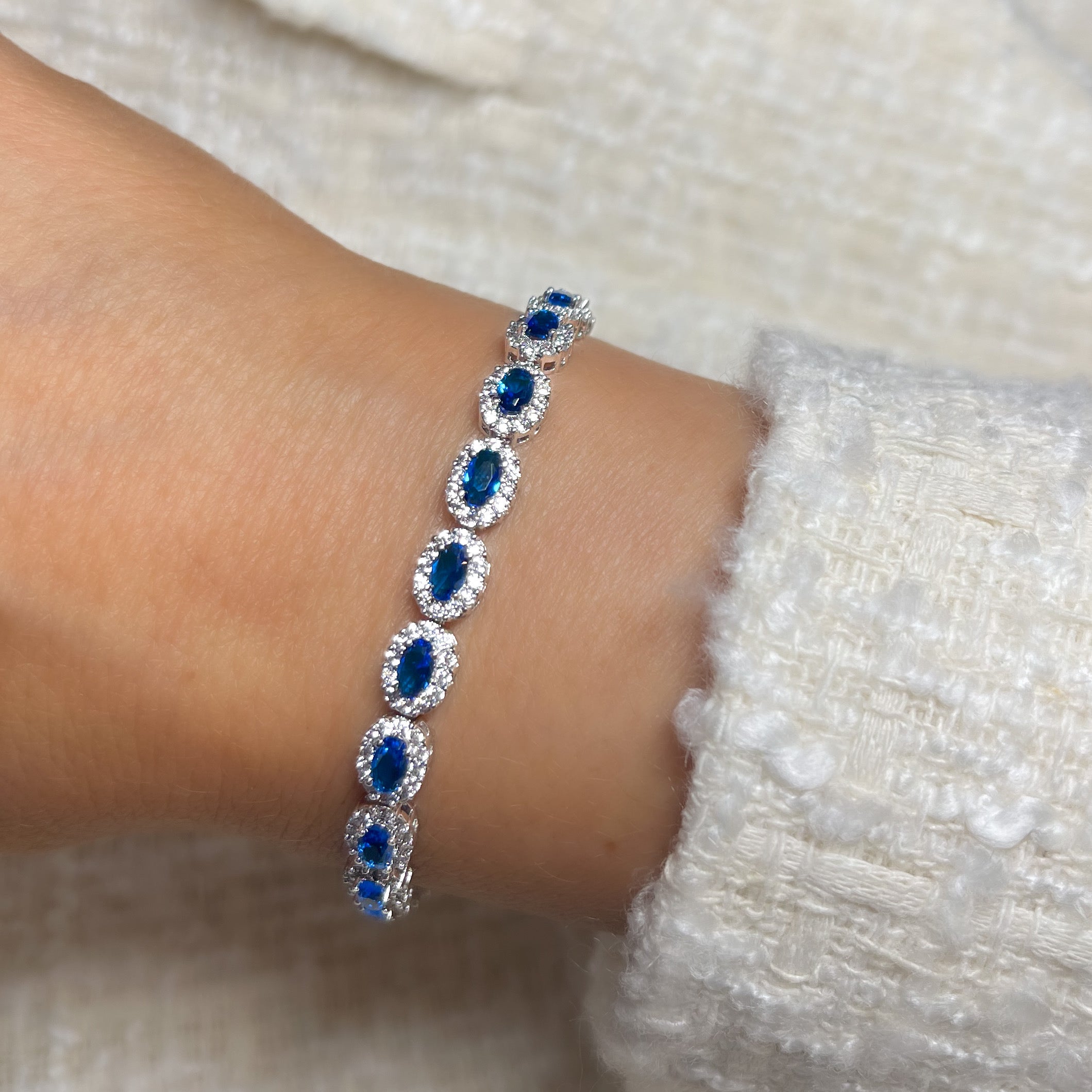 A silver tennis bracelet featuring oval cut blue crystals surrounded by white cubic zirconia.