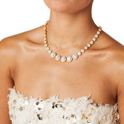 Model wearing a gold crystal tennis necklace featuring graduated cubic zirconia stones with pavé halos, styled with a minimalist outfit to highlight the necklace's elegant sparkle