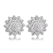 A pair of silver-plated stud earrings arranged side by side on a white background. Each earring is shaped like a stylised flower, featuring a central cluster of round-cut, brilliant cubic zirconia stones. Surrounding the center are two layers of sparkling CZ: an inner ring of smaller round stones, followed by an outer ring of marquise-shaped stones forming petals. The earrings measure approximately 1.6 cm in diameter and reflect light with a lustrous, glittering effect.