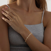 A delicate gold‑plated link bracelet featuring a whimsical parade of stylised elephant silhouettes, each linked trunk-to-tail. The small elephant charms are uniformly sized with softly rounded bodies and upturned trunks, creating a playful, continuous chain. The bracelet is secured with an integrated box‑style clasp and lays flat when worn, measuring around 18 cm in length. The polished gold finish gives a warm, refined sheen, enhancing its charming, artisan-crafted look.