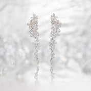 Silver long drop earrings with cascading floral embellishments, tapering to a delicate point; sparkling statement jewelry perfect for weddings, holidays, and special occasions.