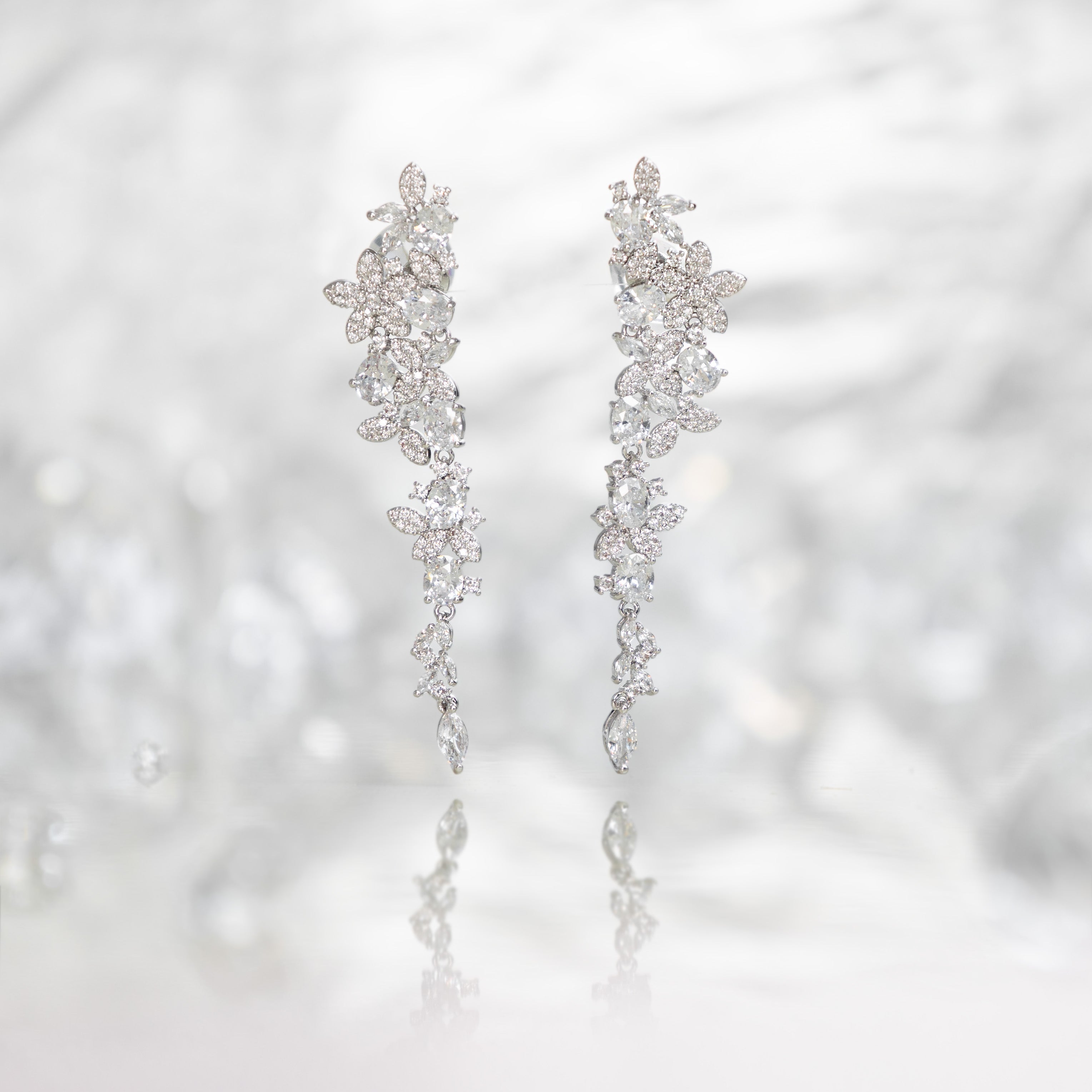 Silver long drop earrings with cascading floral embellishments, tapering to a delicate point; sparkling statement jewelry perfect for weddings, holidays, and special occasions.