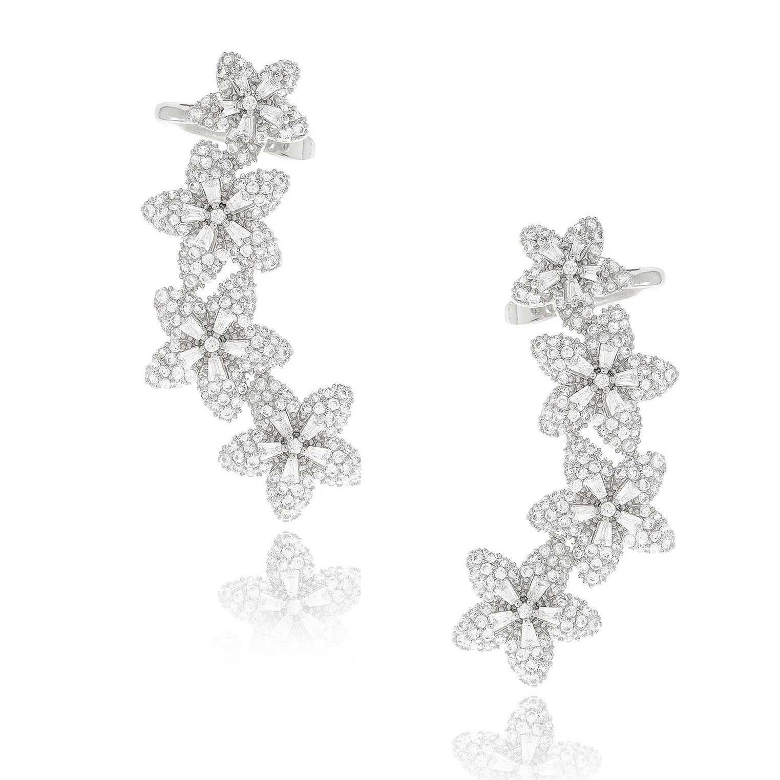 A pair of rhodium-plated ear climbers arranged symmetrically on a white background. Each earring features a graceful, curved line of four stylised flower motifs that follow the ear’s contour. The flowers are fully pavé-set with round cubic zirconia crystals, with one slightly larger bloom at the bottom transitioning to smaller blossoms toward the top. The climbers measure approximately 4.1 cm in height and 2.3 cm in width, and are secured via a long post at the base and a secondary backing near the top to