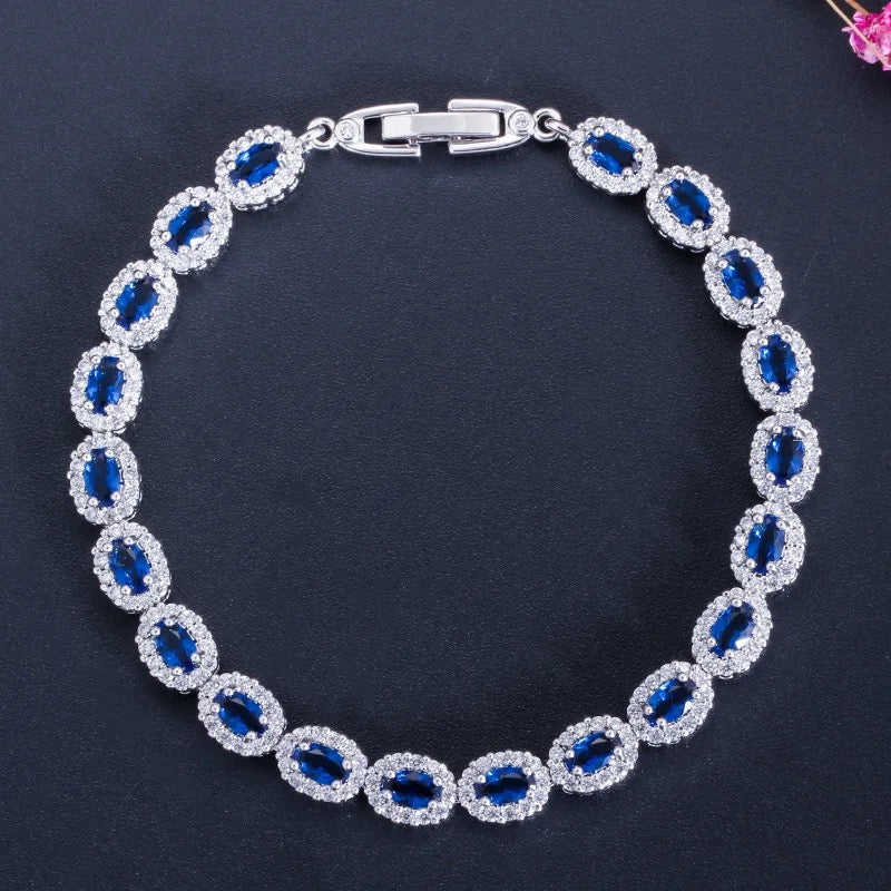 A silver tennis bracelet featuring oval cut blue crystals surrounded by white cubic zirconia.