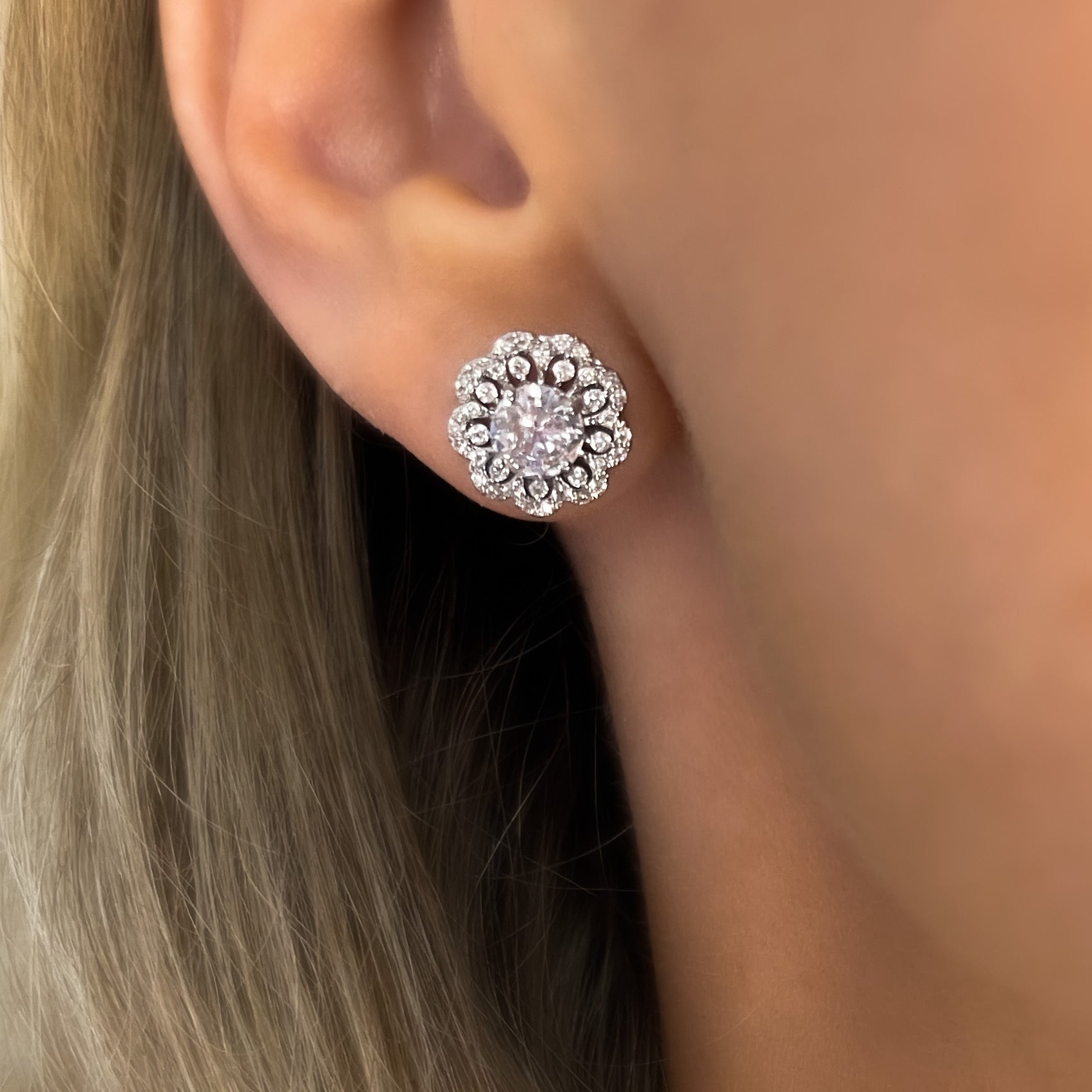 A pair of silver stud earrings with a floral lace edge design, featuring multiple small round cut gems.