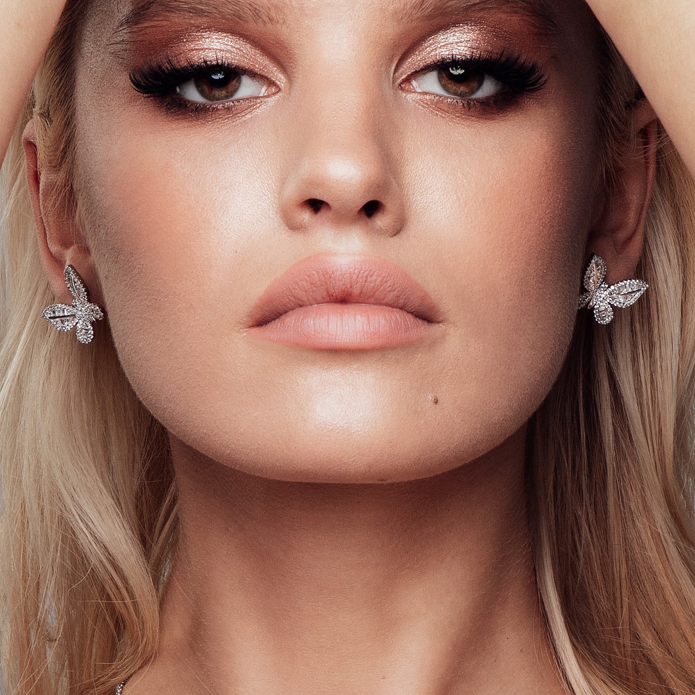 A pair of silver‑plated stud earrings in the shape of delicate butterflies, shown side by side on a white surface. Each earring features a symmetrical butterfly silhouette with gently curved wings. The wings are adorned with tiny pavé-set cubic zirconia crystals that catch the light, while the central body is polished metal. The earrings are compact—approximately 0.8–1 cm across—and fasten with standard push-back posts. The overall design is feminine, sparkling, and refined, making these studs an elegant ye