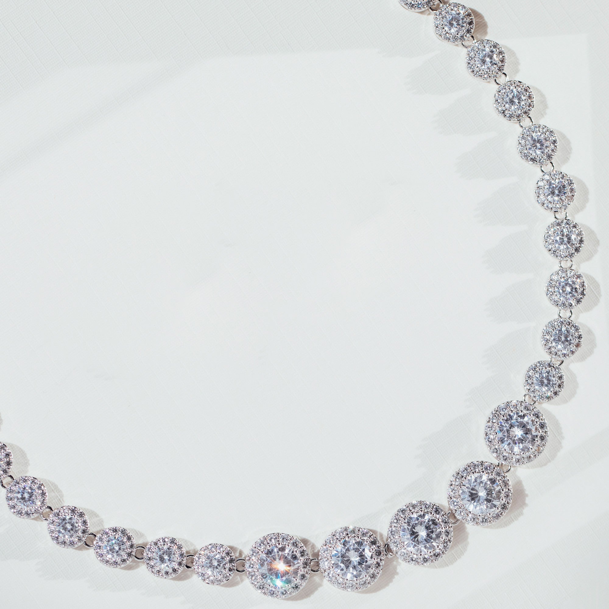 Silver crystal tennis necklace with graduated cubic zirconia stones haloed by pavé, rhodium-plated brass, displayed on a clean white background