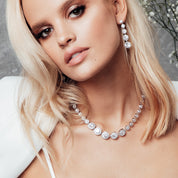 Model wearing a silver crystal tennis necklace featuring graduated cubic zirconia stones with halo pavé detailing, styled against a simple outfit to emphasize the necklace’s elegant sparkle