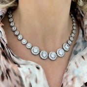 Model wearing a silver crystal tennis necklace featuring graduated cubic zirconia stones with halo pavé detailing, styled against a simple outfit to emphasize the necklace’s elegant sparkle