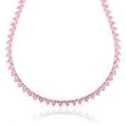 A rose‑gold plated tennis‑style necklace drapes elegantly around a model’s neck. The piece features a continuous row of blush‑pink, heart‑shaped cubic zirconia stones, each approximately 5 mm wide, linked closely together. The necklace measures about 17 in (43 cm) with a 0.5 in extender and fastens with a secure clasp. The polished rose‑gold setting enhances the sparkle of the pink hearts, creating a romantic, feminine shimmer perfect for both everyday wear and special occasions.
