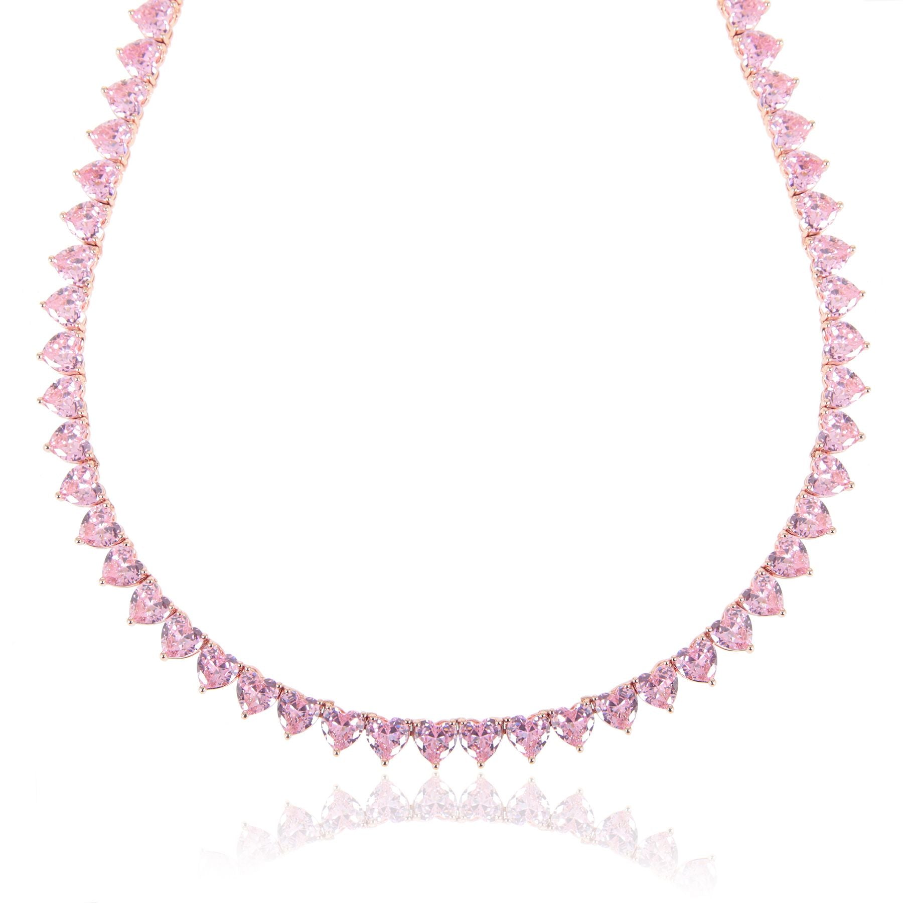 A rose‑gold plated tennis‑style necklace drapes elegantly around a model’s neck. The piece features a continuous row of blush‑pink, heart‑shaped cubic zirconia stones, each approximately 5 mm wide, linked closely together. The necklace measures about 17 in (43 cm) with a 0.5 in extender and fastens with a secure clasp. The polished rose‑gold setting enhances the sparkle of the pink hearts, creating a romantic, feminine shimmer perfect for both everyday wear and special occasions.