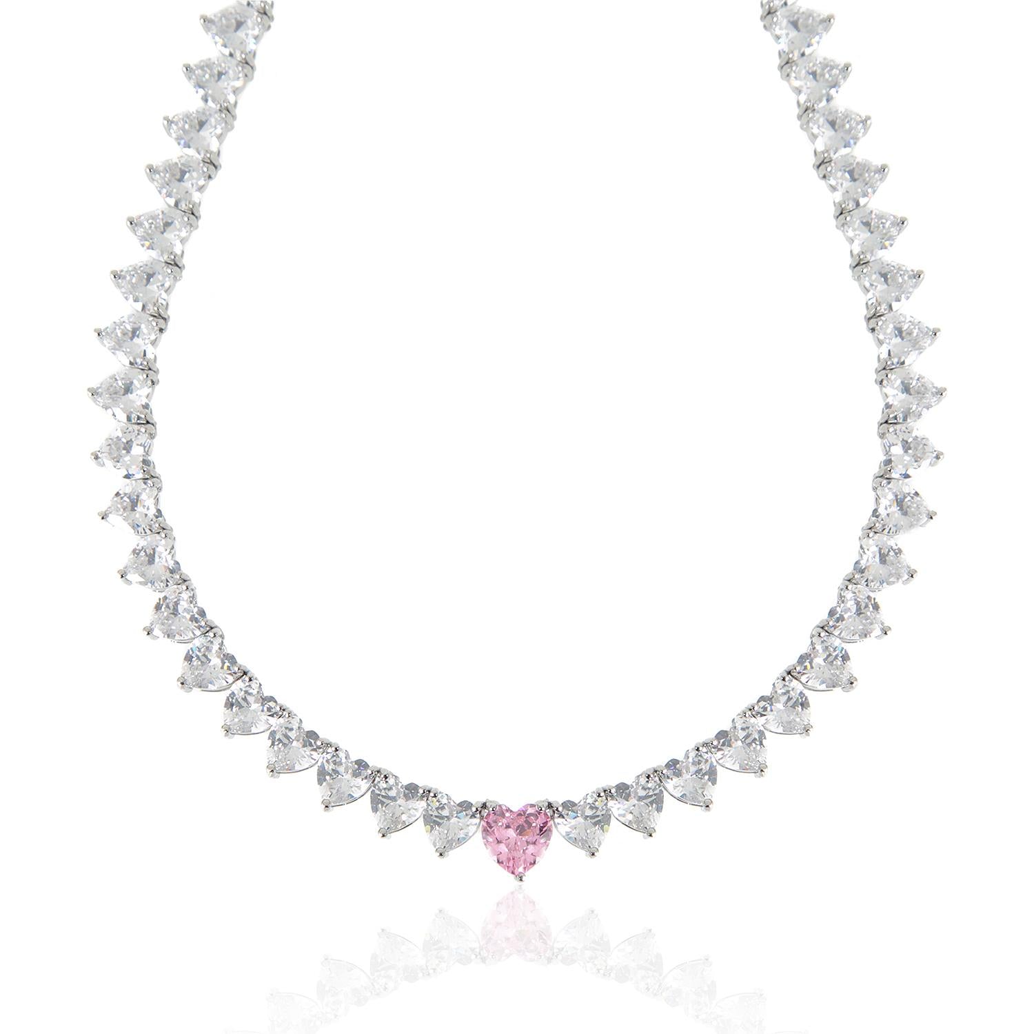 A sparkling silver-plated tennis-style necklace elegantly displayed on a soft, light background. It features a continuous row of heart-shaped cubic zirconia stones, each approximately 7 mm wide, set in rhodium-plated brass. The centerpiece is a single blush-pink heart stone (about 8 mm) that adds a pop of colour. The hearts are closely linked, creating a seamless chain around the neckline, and the full length is approximately 44 cm (17.5”) with a short extender. The polished silver setting enhances the bril