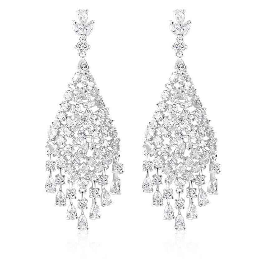 Silver chandelier earrings featuring cascading white cubic zirconia stones, rhodium-plated with a 6.4 cm drop, shown on model and against light and dark backgrounds.