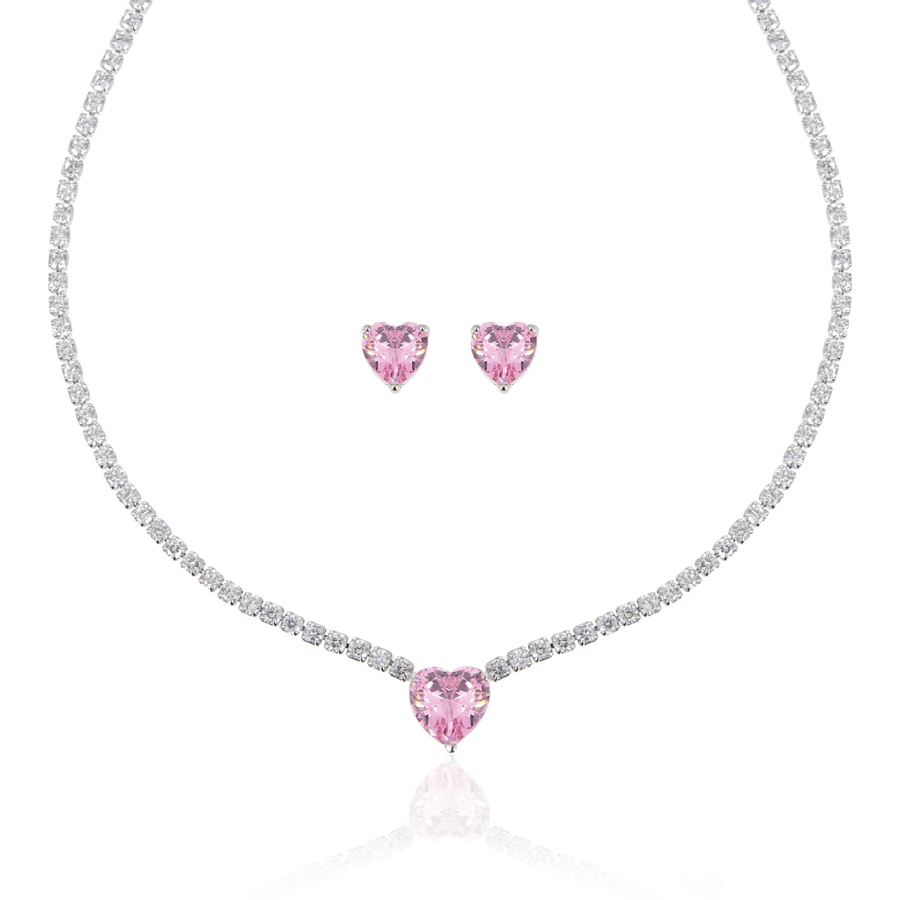 A matching set featuring a delicate silver-plated tennis‑style necklace and coordinating stud earrings displayed on a white background. The necklace consists of a continuous row of small, round white cubic zirconia stones (approximately 2–3 mm each), set in closely linked round bezels. At its centre hangs a single blush-pink, heart-shaped CZ pendant measuring about 8 mm across. Below the necklace, the set includes a pair of matching heart-shaped stud earrings in the same blush-pink tone, each about 8 mm dia