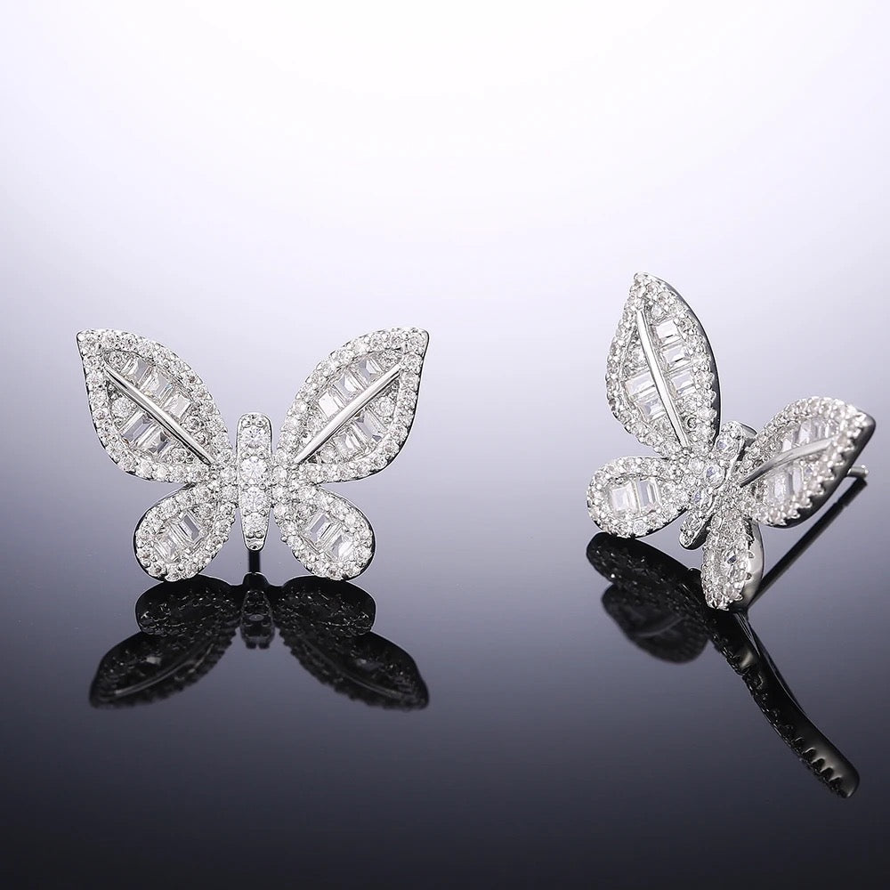 A pair of silver‑plated stud earrings in the shape of delicate butterflies, shown side by side on a white surface. Each earring features a symmetrical butterfly silhouette with gently curved wings. The wings are adorned with tiny pavé-set cubic zirconia crystals that catch the light, while the central body is polished metal. The earrings are compact—approximately 0.8–1 cm across—and fasten with standard push-back posts. The overall design is feminine, sparkling, and refined, making these studs an elegant ye