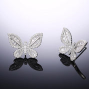 A pair of silver‑plated stud earrings in the shape of delicate butterflies, shown side by side on a white surface. Each earring features a symmetrical butterfly silhouette with gently curved wings. The wings are adorned with tiny pavé-set cubic zirconia crystals that catch the light, while the central body is polished metal. The earrings are compact—approximately 0.8–1 cm across—and fasten with standard push-back posts. The overall design is feminine, sparkling, and refined, making these studs an elegant ye