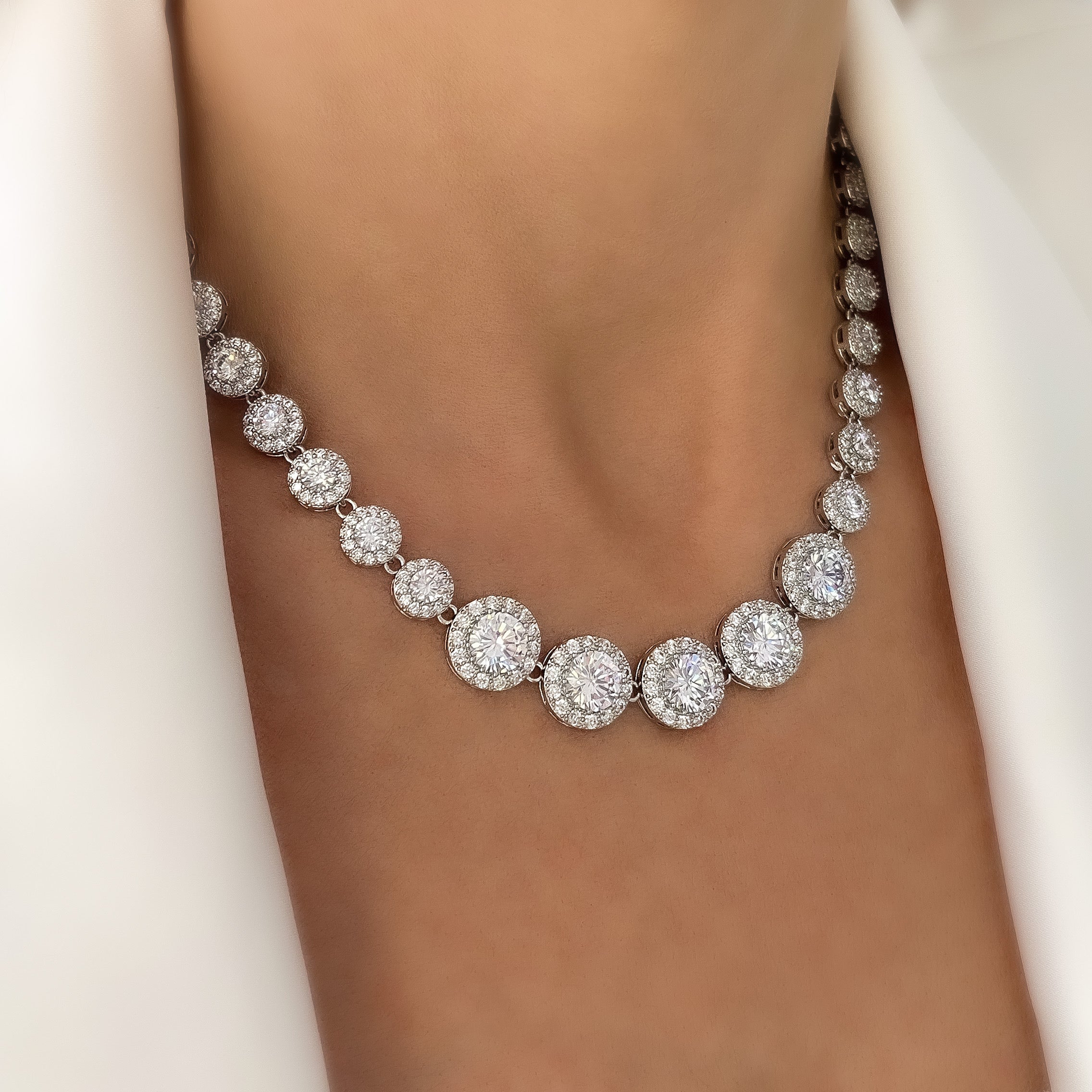 Model wearing a silver crystal tennis necklace featuring graduated cubic zirconia stones with halo pavé detailing, styled against a simple outfit to emphasize the necklace’s elegant sparkle