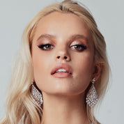 Silver chandelier earrings featuring cascading white cubic zirconia stones, rhodium-plated with a 6.4 cm drop, shown on model and against light and dark backgrounds.