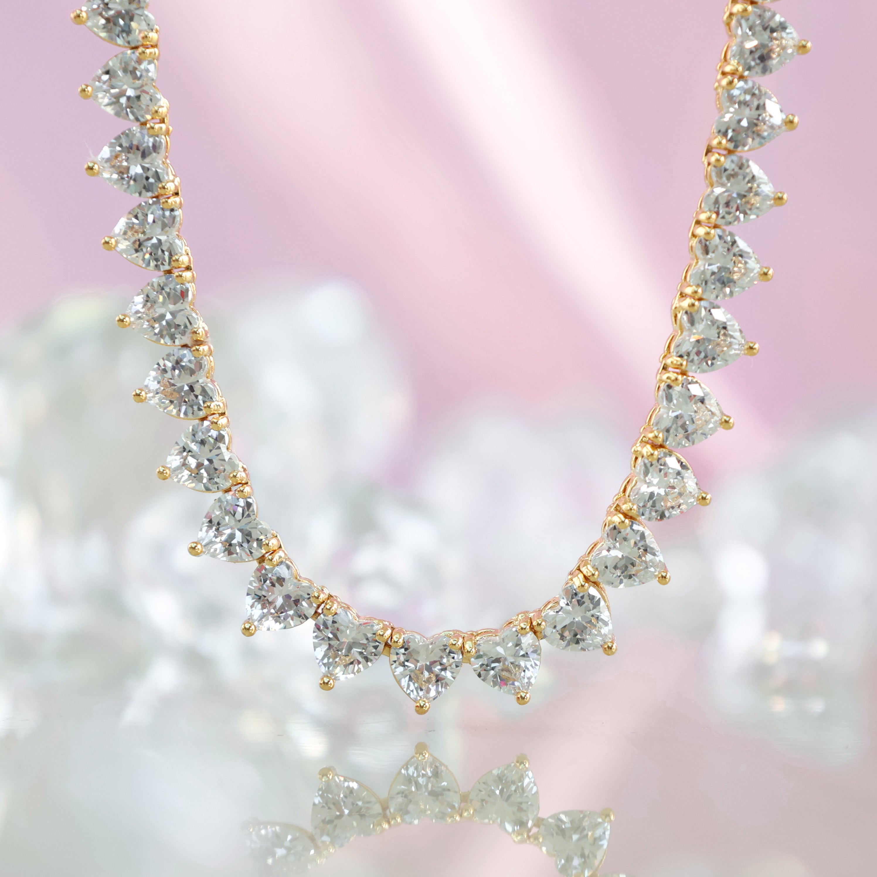 A deluxe tennis-style necklace composed of 7 mm heart-shaped clear cubic zirconia stones, each set in polished 18 ct gold plating. The hearts are aligned closely along a 16‑inch (40 cm) chain, creating a continuous sparkle around the neckline. The design features a secure, invisible clasp hidden behind one stone for a seamless look. The high-reflective gold finish and perfectly cut CZs give the piece a luxurious, radiant appeal—ideal for special occasions or elevating everyday style. It weighs approximately