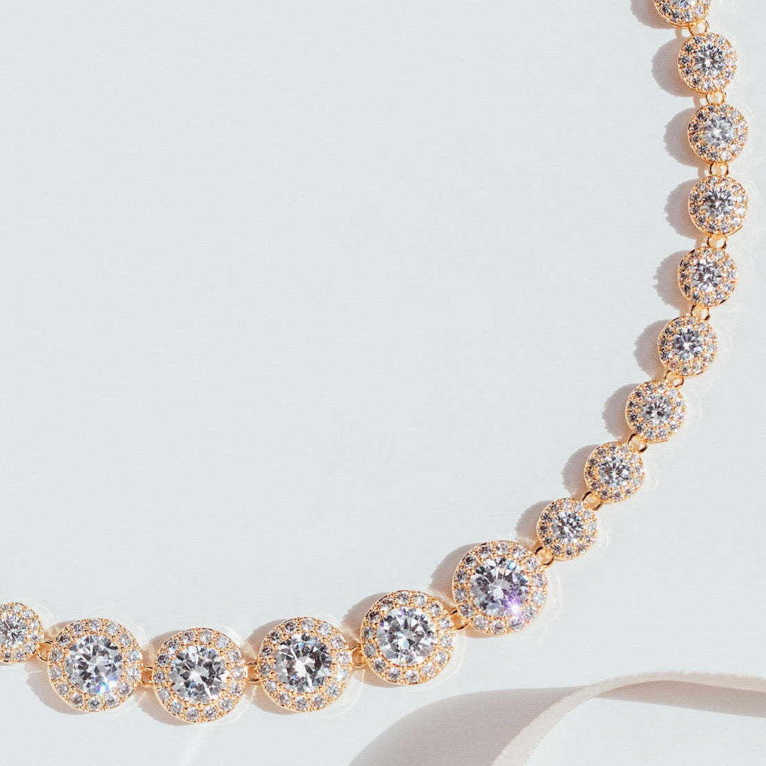 gold crystal tennis necklace with graduated cubic zirconia stones and pavé halos, photographed against a white background to highlight the necklace’s radiant sparkle and elegant design