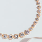 gold crystal tennis necklace with graduated cubic zirconia stones and pavé halos, photographed against a white background to highlight the necklace’s radiant sparkle and elegant design