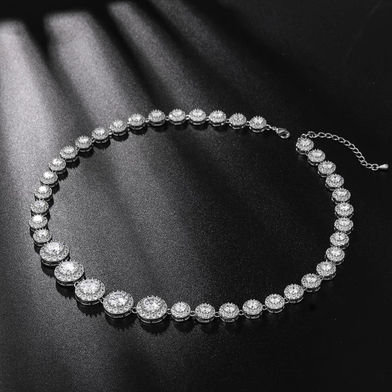 Silver crystal tennis necklace with graduated cubic zirconia stones haloed by pavé, rhodium-plated brass, displayed on a clean black background