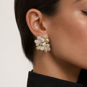 A close-up of a model's ear wearing a floral stud earring with yellow-green and white stones, set against a light neutral background.