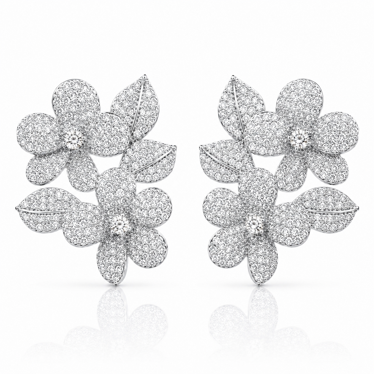 A pair of silver-toned pavé flower stud earrings with leaf details, set with small clear stones and photographed on a clean white background with a soft reflection below.