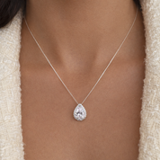 Teardrop-shaped diamond pendant on a necklace against a neutral background