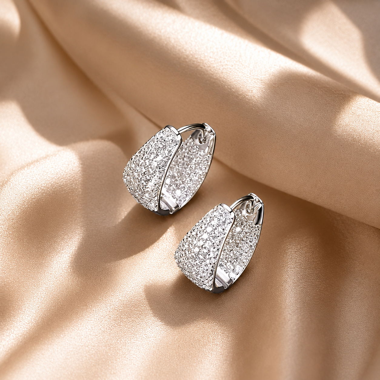 Silver pave hoop earrings with sparkling stones on a beige fabric background