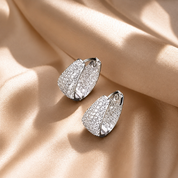 Silver pave hoop earrings with sparkling stones on a beige fabric background