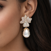 Close-up of a woman wearing a decorative orchid flower earring with a pearl drop. Valentina-Rose Jewellery