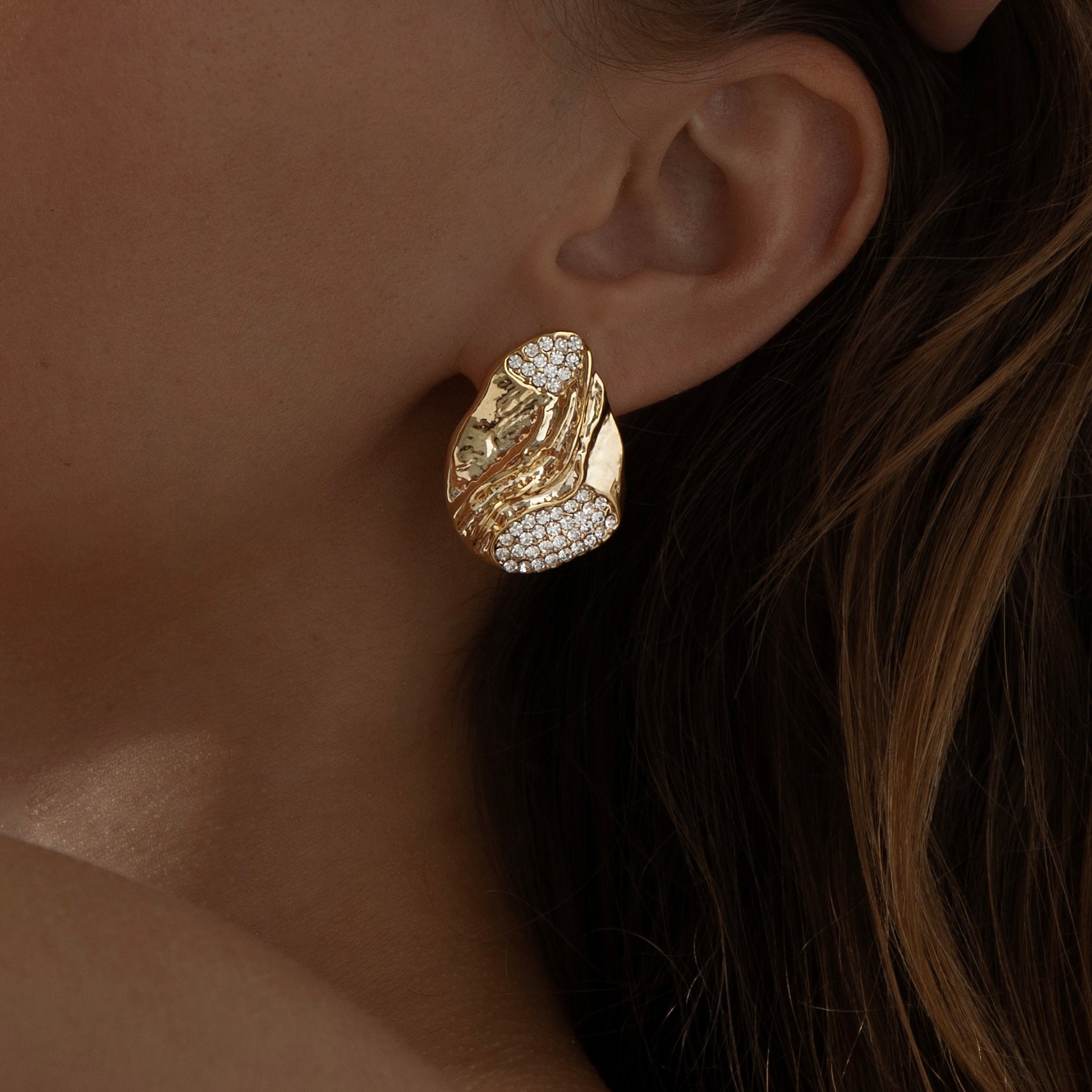 A pair of gold‑plated stud earrings, each shaped like three elegant, tapering wave arches that fan outward in a stylised, goddess-inspired design. The curved strands are smooth, mirror‑polished, and evenly spaced, creating a sense of movement and volume while remaining compact—approximately 1.3 cm tall from post to tip. They appear to sit snugly along the earlobe and fasten with standard push-back posts. The warm metallic sheen and sculptural silhouette evoke a graceful, contemporary luxury vibe.