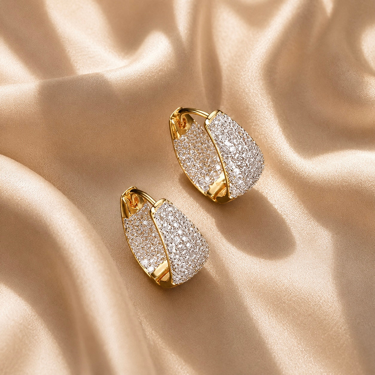 Pave silver huggie hoop earrings on a beige fabric background