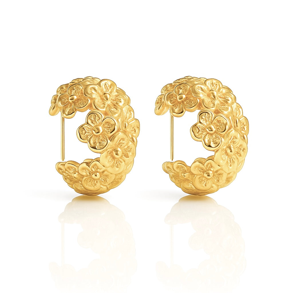 A pair of chunky, semi-circular hoop earrings photographed upright on a white background. Each hoop is crafted from stainless steel plated with glossy 18K gold, featuring an embossed design of small buttercup flowers densely covering the outer surface. The hoops are approximately 2.4 cm tall and 1.8 cm wide, with a smooth, reflective finish. They weigh around 15 g and appear waterproof and tarnish-resistant, making them an everyday-ready, statement floral accessory.