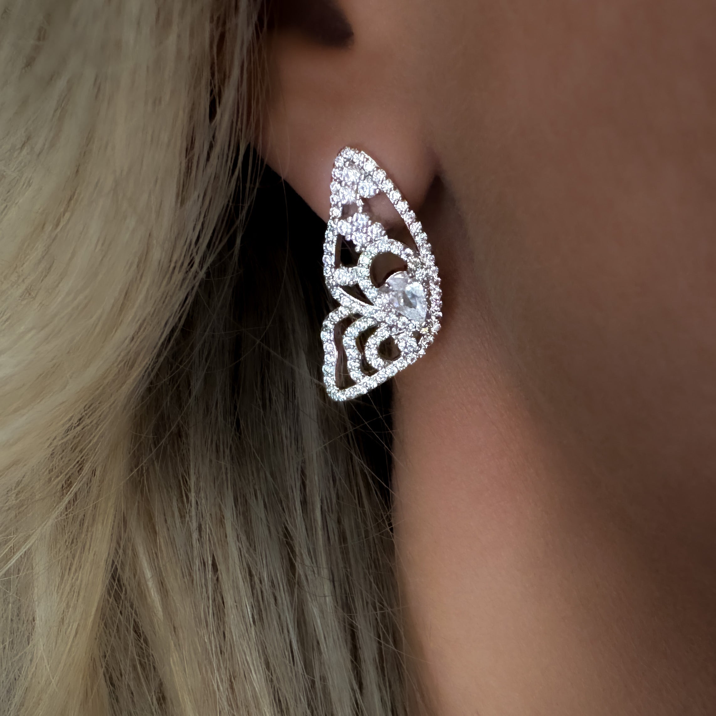 Close-up of a person wearing a silver butterfly-shaped earring with a blurred background