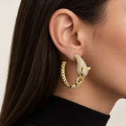 A close-up of a model's ear wearing a gold hoop earring with a detailed leopard head and small green eyes, set with sparkling clear stones.